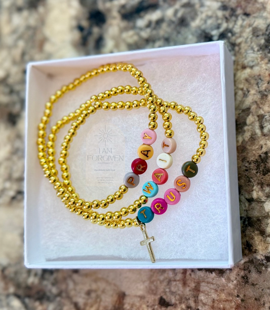 Gold bracelet with colorful beads on a white card against a marble background